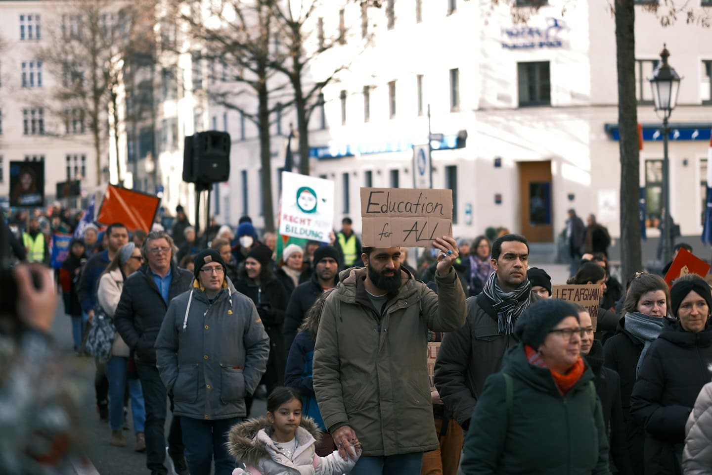 Vielfältige Menschen demonstrieren für Bildung und halten Schilder in einer Stadtstraße.