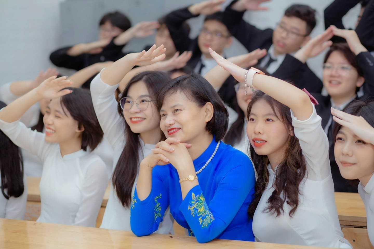 Schüler und Lehrer lächeln mit erhobenen Händen im Klassenzimmer.